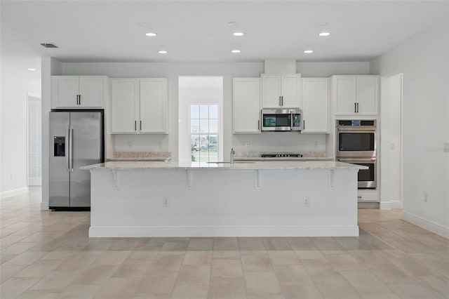 5204 Obsidian Gate Dr, Mount Dora, FL 32757 - kitchen with stainless steel appliances, white cabinetry, light stone counters, a large island with sink, and recessed lighting