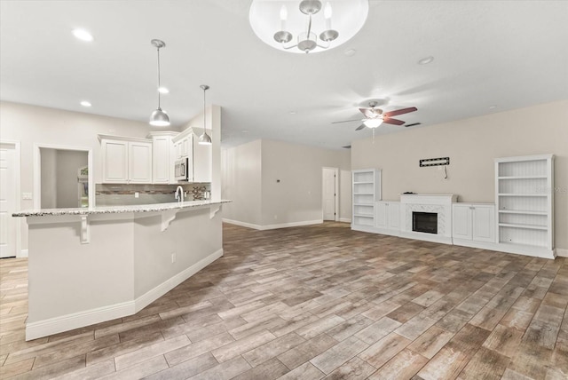 917 Southern Oak Ln, Apopka, FL 32712 - kitchen with stainless steel microwave, light wood-style floors, a kitchen breakfast bar, a ceiling fan, and light stone counters