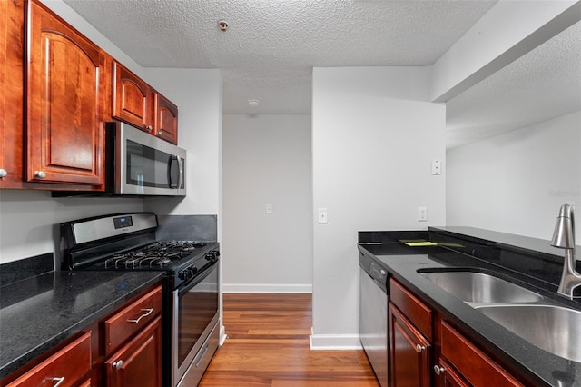2041 Dixie Belle Dr Unit 2041C, Orlando, FL 32812 - kitchen with appliances with stainless steel finishes, wood finished floors, a textured ceiling, reddish brown cabinets, and dark stone countertops