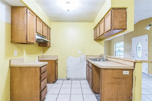 1212 N Hudson St, Orlando, FL 32808 - kitchen featuring light tile patterned flooring, under cabinet range hood, a peninsula, light countertops, and brown cabinetry