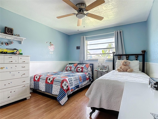 1475 Mars St, Merritt Island, FL 32953 - bedroom with light wood-style floors, a wainscoted wall, a textured ceiling, and ceiling fan