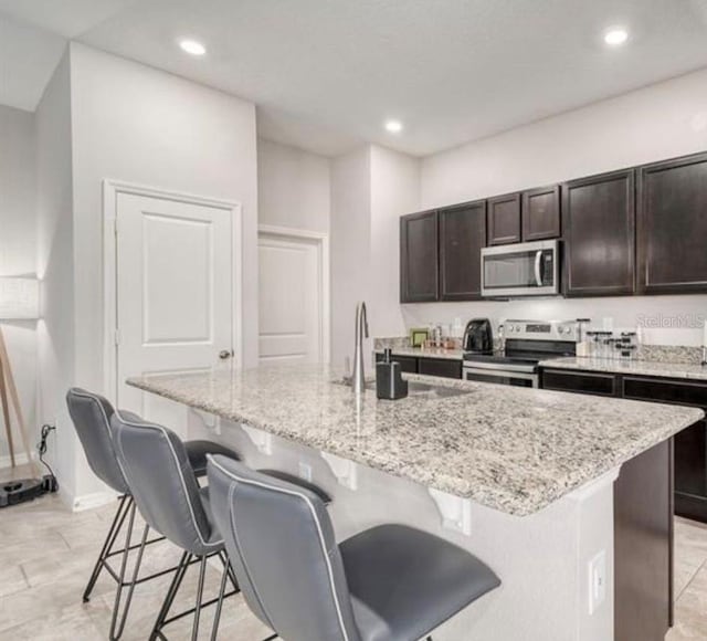 3028 Lakes Crest Ave, Saint Cloud, FL 34772 - kitchen with appliances with stainless steel finishes, a center island with sink, a kitchen bar, light stone countertops, and recessed lighting