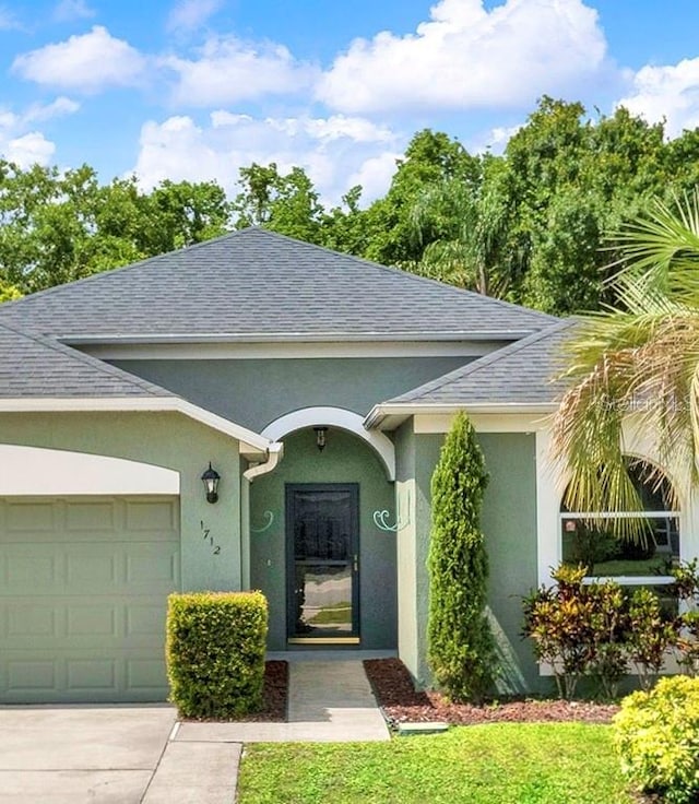 1712 Riveredge Rd, Oviedo, FL 32766 - doorway to property featuring stucco siding, an attached garage, roof with shingles, and driveway