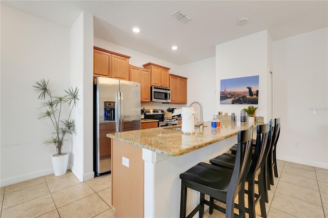 3193 Pequod Pl, Kissimmee, FL 34746 - kitchen featuring appliances with stainless steel finishes, light stone counters, a kitchen breakfast bar, light tile patterned floors, and a peninsula