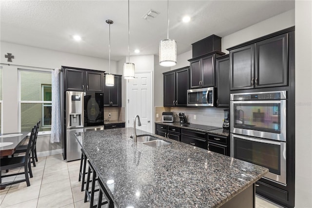 14536 Golden Harbor Ln, Winter Garden, FL 34787 - kitchen with appliances with stainless steel finishes, decorative backsplash, a kitchen island with sink, dark stone counters, and recessed lighting