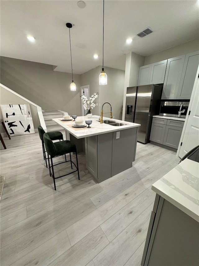 1526 Hempel Ave, Gotha, FL 34734 - kitchen featuring appliances with stainless steel finishes, gray cabinets, light wood-style flooring, a kitchen island with sink, and hanging light fixtures