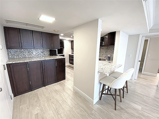2400 Presidential Way Unit 1104, West Palm Beach, FL 33401 - kitchen featuring light wood-style flooring, a kitchen breakfast bar, tasteful backsplash, dark brown cabinetry, and light stone counters