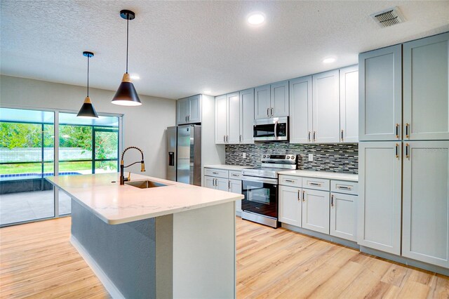 5938 Marlberry Dr, Orlando, FL 32819 - kitchen with stainless steel appliances, light wood-type flooring, tasteful backsplash, a textured ceiling, and a kitchen island with sink