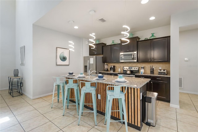 2108 Morocco Way, Kissimmee, FL 34747 - kitchen featuring appliances with stainless steel finishes, a center island with sink, backsplash, light tile patterned floors, and a breakfast bar area