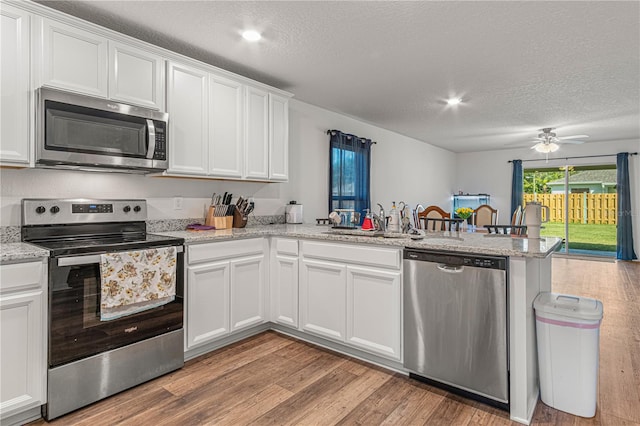 13 Ryken Ln, Palm Coast, FL 32164 - kitchen with appliances with stainless steel finishes, a peninsula, a textured ceiling, light wood-style flooring, and white cabinetry