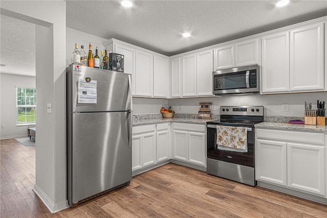 13 Ryken Ln, Palm Coast, FL 32164 - kitchen featuring appliances with stainless steel finishes, a textured ceiling, white cabinetry, light wood-type flooring, and light stone countertops