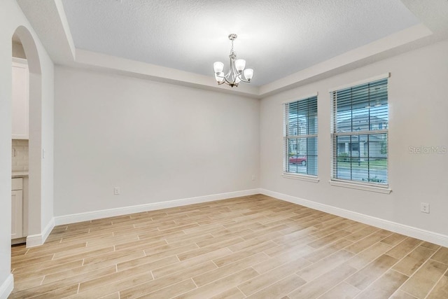 16146 Point Rock Dr, Winter Garden, FL 34787 - unfurnished room featuring a tray ceiling, light wood-style floors, a chandelier, arched walkways, and a textured ceiling