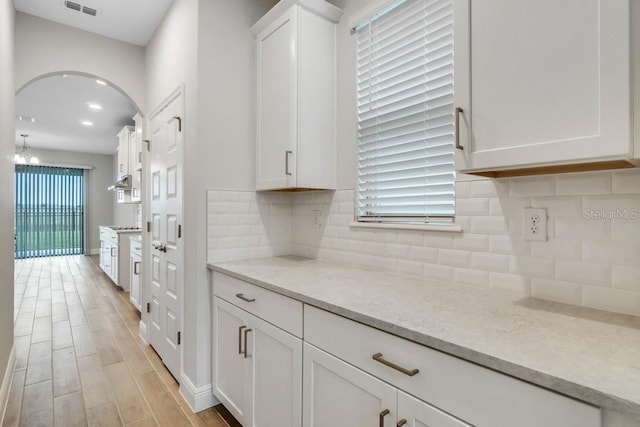 16146 Point Rock Dr, Winter Garden, FL 34787 - kitchen featuring white cabinetry, light wood finished floors, tasteful backsplash, and light stone counters