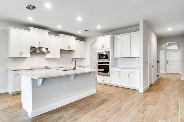 16146 Point Rock Dr, Winter Garden, FL 34787 - kitchen featuring stainless steel appliances, under cabinet range hood, arched walkways, light countertops, and light wood-style flooring