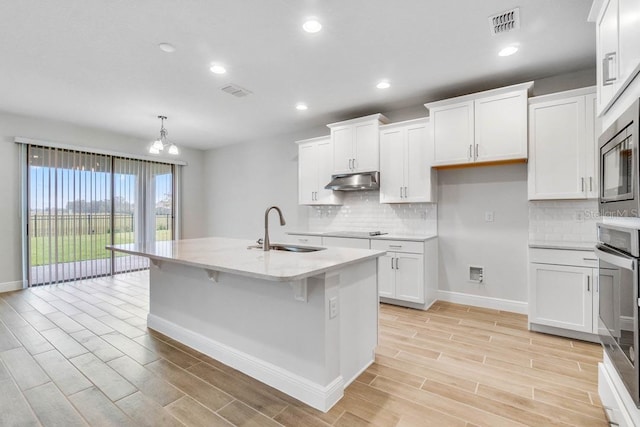 16146 Point Rock Dr, Winter Garden, FL 34787 - kitchen with light wood finished floors, white cabinets, tasteful backsplash, stainless steel appliances, and under cabinet range hood
