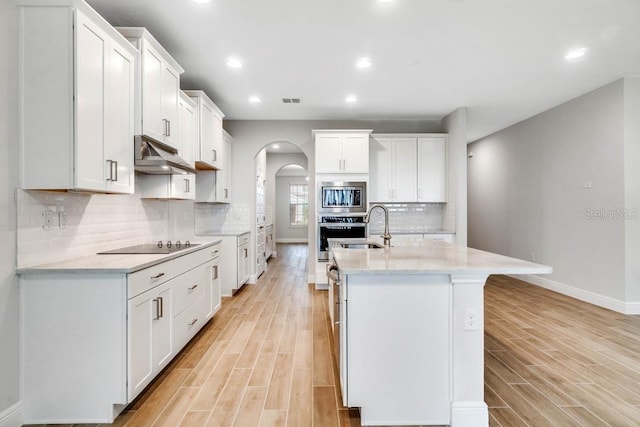 16146 Point Rock Dr, Winter Garden, FL 34787 - kitchen featuring stainless steel appliances, arched walkways, under cabinet range hood, light wood-style floors, and an island with sink