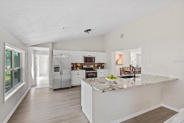 370 Hand Ave, Ormond Beach, FL 32174 - kitchen featuring stainless steel appliances, vaulted ceiling, a peninsula, white cabinetry, and light stone countertops