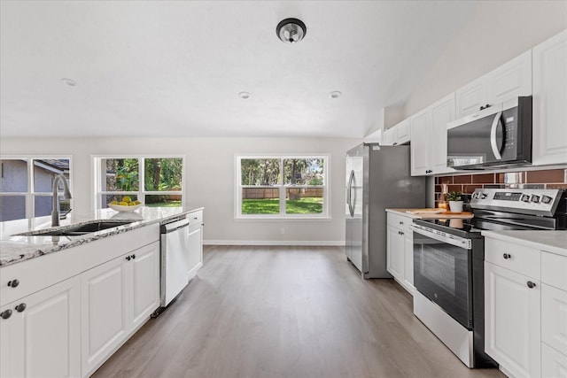 370 Hand Ave, Ormond Beach, FL 32174 - kitchen with appliances with stainless steel finishes, light wood finished floors, white cabinetry, tasteful backsplash, and vaulted ceiling