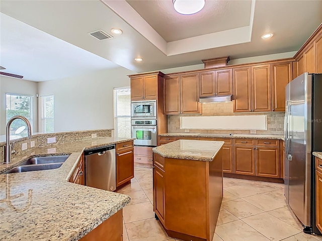 2209 Callaway Ct, Davenport, FL 33837 - kitchen featuring stainless steel appliances, a kitchen island, under cabinet range hood, decorative backsplash, and a tray ceiling