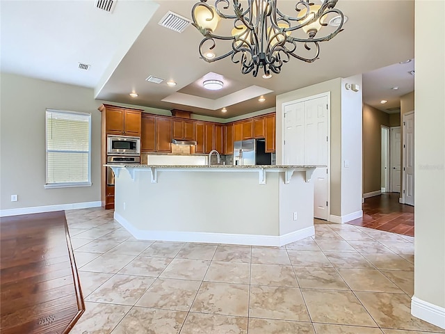 2209 Callaway Ct, Davenport, FL 33837 - kitchen with appliances with stainless steel finishes, a tray ceiling, brown cabinetry, and a kitchen bar