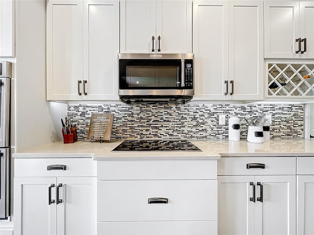 31980 Geoff Way, Sorrento, FL 32776 - kitchen with stainless steel microwave, cooktop, light countertops, white cabinetry, and backsplash