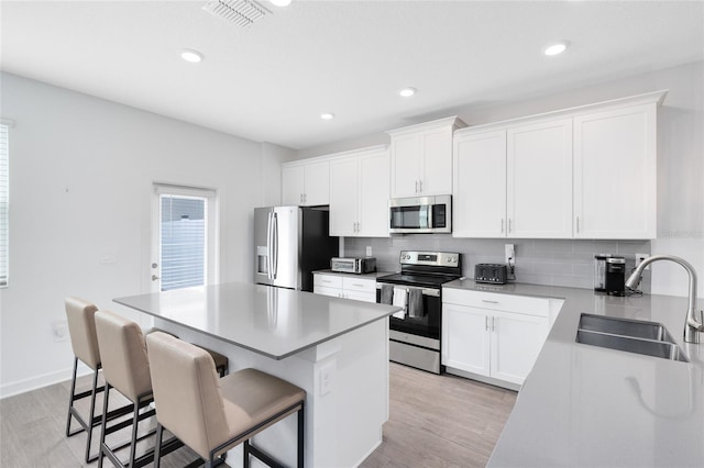 3099 Ella Way, Saint Cloud, FL 34771 - kitchen with stainless steel appliances, light wood-type flooring, a kitchen island, a breakfast bar, and white cabinets