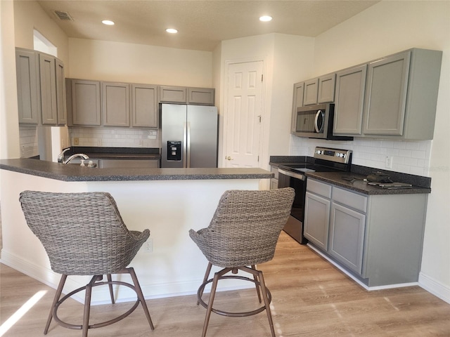 152 Glendale Ct, Kissimmee, FL 34759 - kitchen with stainless steel appliances, a peninsula, dark countertops, tasteful backsplash, and light wood-type flooring