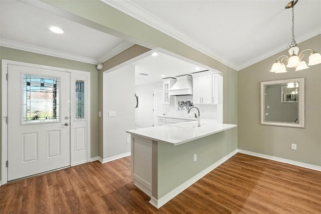 2895 Apache Ct, The Villages, FL 32163 - kitchen featuring premium range hood, dark wood-style floors, white cabinets, a peninsula, and ornamental molding