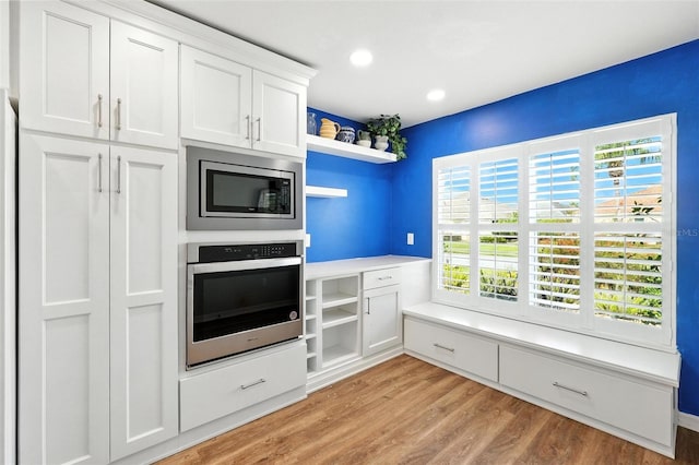 2895 Apache Ct, The Villages, FL 32163 - kitchen featuring appliances with stainless steel finishes, open shelves, white cabinets, light wood-style flooring, and healthy amount of natural light