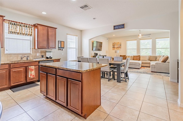1639 Balsam Willow Trl, Orlando, FL 32825 - kitchen with arched walkways, light stone countertops, a kitchen island, a ceiling fan, and light tile patterned floors