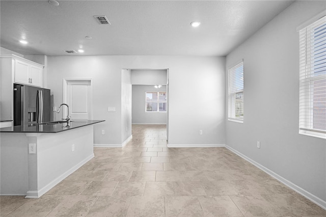 6449 Sprucepine Ln, Saint Cloud, FL 34771 - kitchen featuring stainless steel refrigerator with ice dispenser, dark countertops, white cabinetry, recessed lighting, and an island with sink