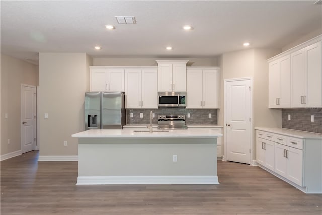 2833 E Newhaven St, Inverness, FL 34453 - kitchen featuring appliances with stainless steel finishes, decorative backsplash, an island with sink, white cabinets, and wood finished floors