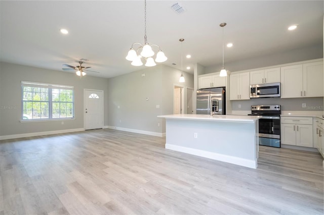 kitchen with appliances with stainless steel finishes, light countertops, a kitchen island with sink, ceiling fan, and a chandelier
