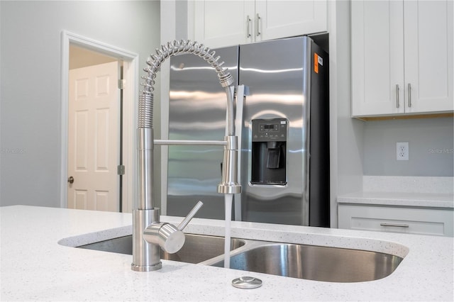 kitchen with stainless steel refrigerator with ice dispenser, light stone counters, and white cabinets