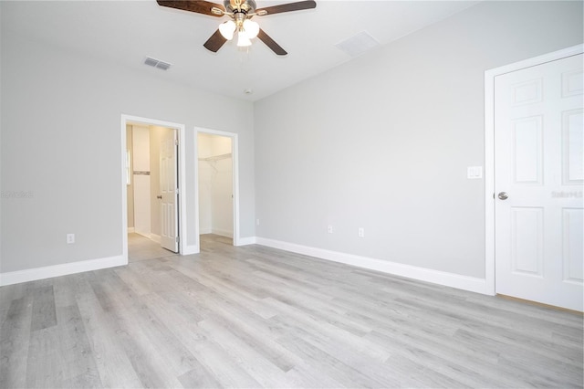 unfurnished bedroom featuring light wood-style flooring, a walk in closet, a closet, and a ceiling fan