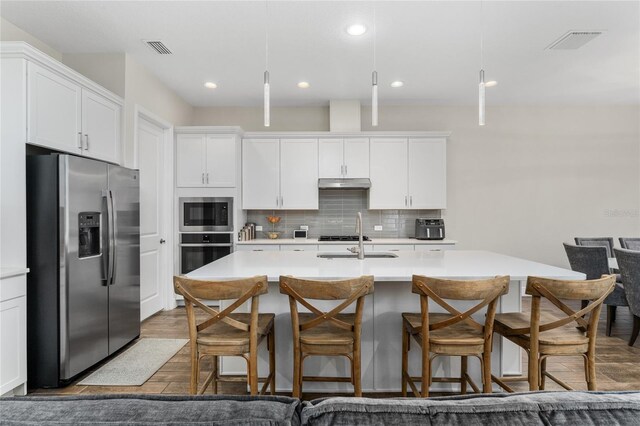 15716 Sweet Lemon Way, Winter Garden, FL 34787 - kitchen featuring appliances with stainless steel finishes, under cabinet range hood, light countertops, a kitchen island with sink, and decorative backsplash