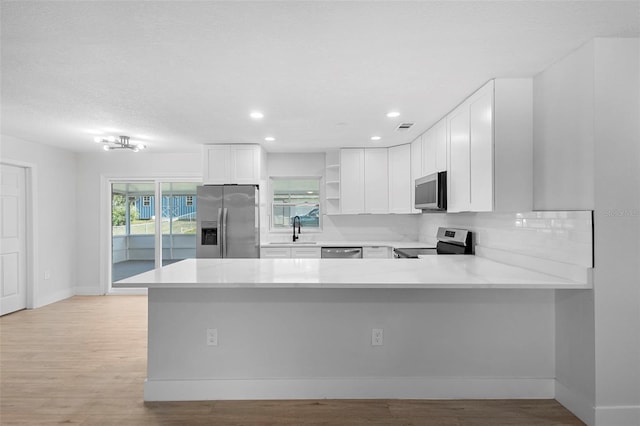 105 E Magnolia St, Davenport, FL 33837 - kitchen featuring appliances with stainless steel finishes, open shelves, light countertops, light wood-style floors, and white cabinets