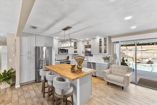 2356 Date Palm Dr, Edgewater, FL 32141 - kitchen featuring stainless steel appliances, wood counters, light wood-style flooring, a kitchen breakfast bar, and glass insert cabinets