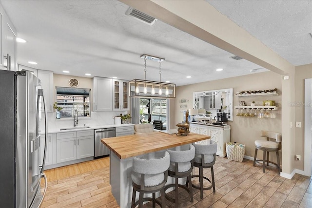 2356 Date Palm Dr, Edgewater, FL 32141 - kitchen with appliances with stainless steel finishes, wooden counters, light wood-style floors, a kitchen bar, and glass insert cabinets