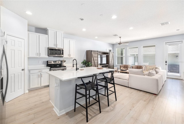 8164 Wood Sage Dr, Winter Garden, FL 34787 - kitchen featuring appliances with stainless steel finishes, a breakfast bar, open floor plan, recessed lighting, and light wood-style flooring