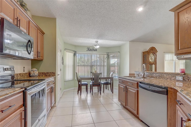 2800 Woodsmere Ct, Kissimmee, FL 34746 - kitchen featuring stainless steel appliances, a textured ceiling, brown cabinetry, light stone countertops, and a peninsula