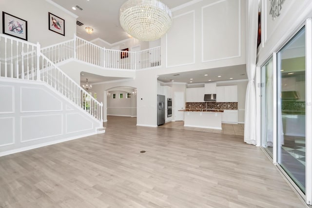 5552 Remsen Cay Ln, Windermere, FL 34786 - unfurnished living room featuring a chandelier, a high ceiling, stairs, light wood-style flooring, and arched walkways