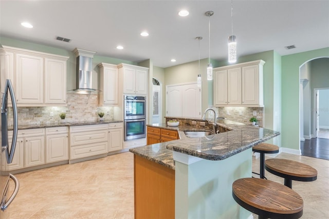 3531 Oriskany Dr, Orlando, FL 32820 - kitchen with wall chimney range hood, stainless steel double oven, backsplash, recessed lighting, and a kitchen bar