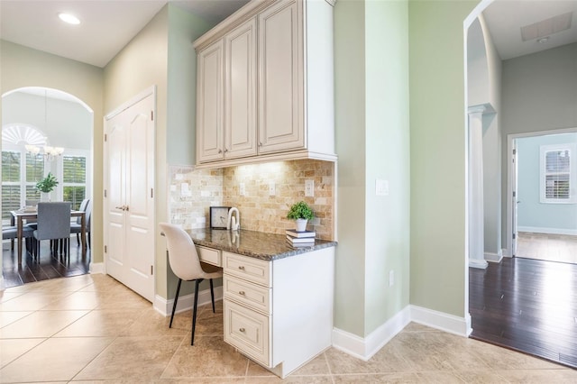 3531 Oriskany Dr, Orlando, FL 32820 - kitchen with arched walkways, a chandelier, dark stone counters, decorative backsplash, and cream cabinets