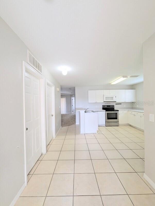 2816 Club Cortile Cir Unit A, Kissimmee, FL 34746 - kitchen with stainless steel range with electric stovetop, white microwave, light countertops, white cabinets, and light tile patterned floors