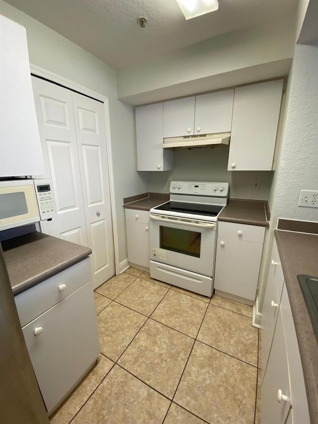 kitchen with white appliances, under cabinet range hood, dark countertops, light tile patterned floors, and white cabinetry