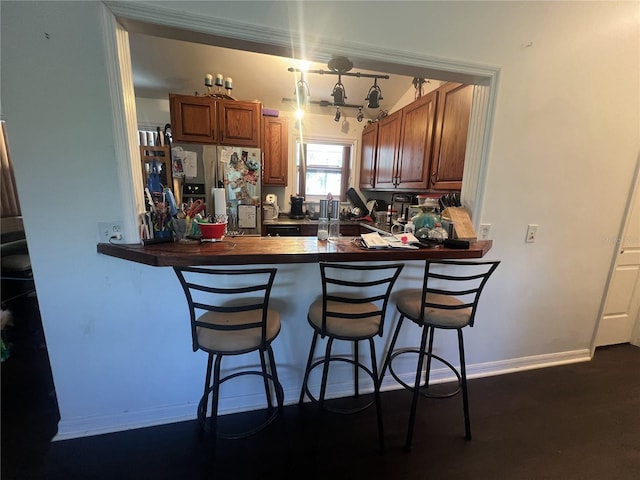 3767 Hibiscus St, Big Pine Key, FL 33043 - kitchen with stainless steel fridge with ice dispenser, dark countertops, a peninsula, brown cabinets, and a kitchen bar