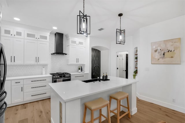 215 Foxglove Way, Deland, FL 32724 - kitchen featuring wall chimney exhaust hood, stainless steel gas range, light wood-style floors, arched walkways, and backsplash