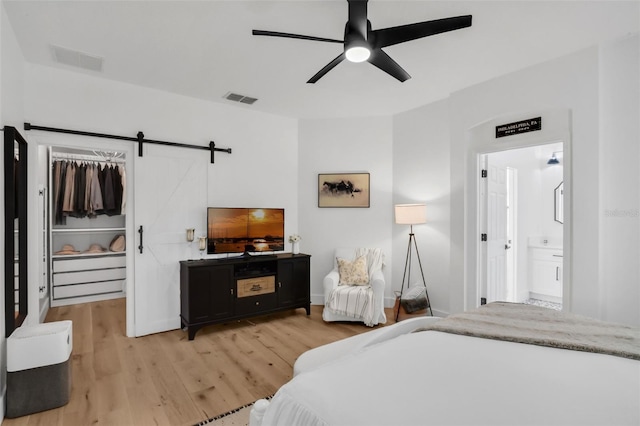215 Foxglove Way, Deland, FL 32724 - bedroom with a barn door, a spacious closet, light wood-style floors, connected bathroom, and a ceiling fan
