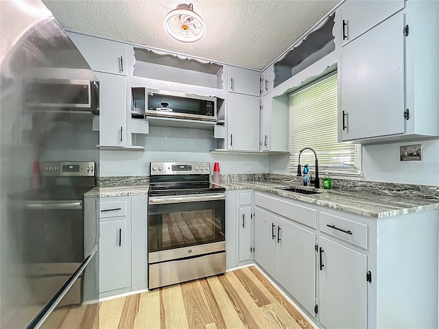 207 Kay St, Auburndale, FL 33823 - kitchen featuring stainless steel appliances, light wood finished floors, a textured ceiling, open shelves, and light stone countertops